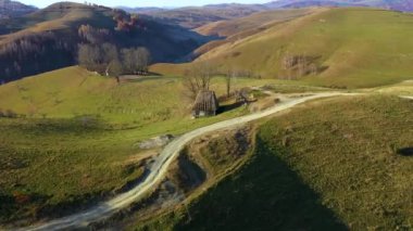 Sonbahar kırsal dağ manzarası ile ahşap evler, thatched çatı ve toprak yola Transilvanya, Romanya hava dron 4k görünümü
