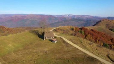 Sonbahar kırsal dağ manzarası ile ahşap evler, thatched çatı ve toprak yola Transilvanya, Romanya hava dron 4k görünümü