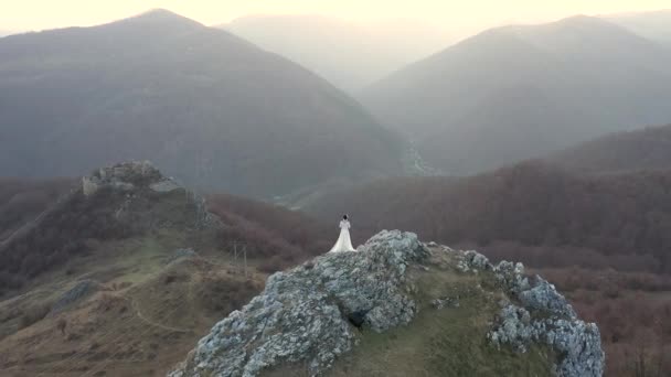 崖の上に立っている白いウェディング ドレスの花嫁 空中ドローン — ストック動画