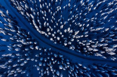 Aerial drone view of slippery road in idyllic, snow covered winter forest