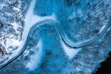 Mavi saat sırasında ormandaki karanlık kış yol. Hava dron görünümü