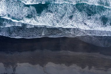 Atlantik okyanusu dalgalarının havadan görünümü siyah kumlu plajı yıkıyor