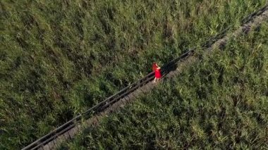  Doğadaki tahta köprü üzerinde çıplak ayakla duran kırmızı elbiseli kadının hava manzarası.