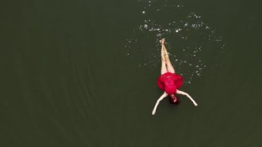   Sakin suda yüzen kırmızı elbiseli muhteşem kadının hava yavaş çekim görüntüsü.