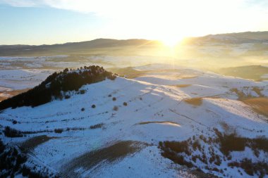 İnsansız hava aracı ile, soğuk kırsal tepelerin üzerindeki günbatımı manzarası.