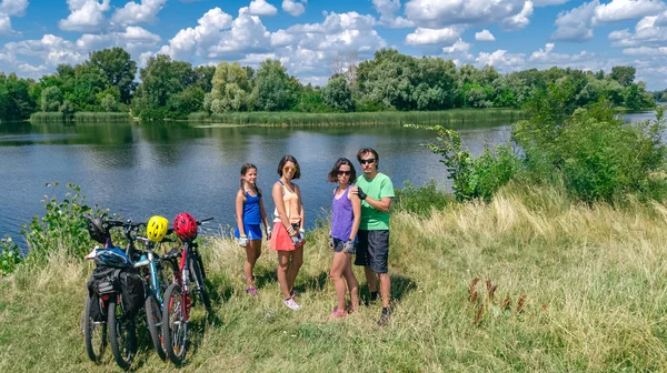 Family on bikes cycling outdoors, active parents and kids on bicycles, aerial view of happy family with children relaxing near beautiful river from above, sport and fitness concept