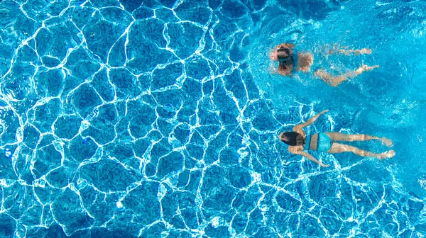 Aerial drone view of girls in swimming pool water from above, active children swim, kids have fun on tropical family vacation, holiday resort concept