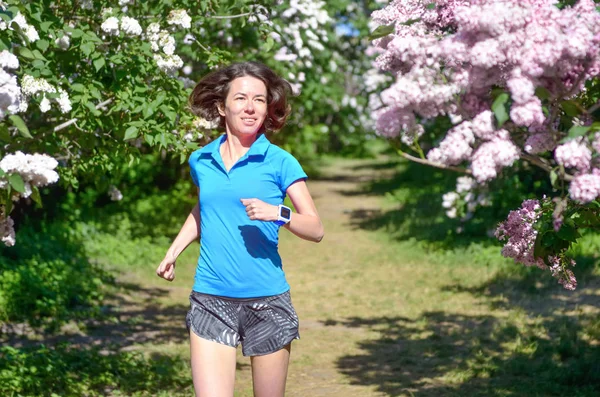 ライラックの花と春の公園でジョギング女性ランナー朝実行アウトドア フィットネスや健康的なライフ スタイルのコンセプトを実行しています — ストック写真