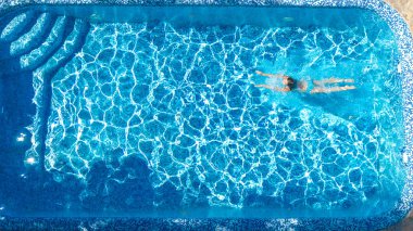Yüzme havuzundaki aktif kız yukarıdan drone görüntüsü, mavi suda yüzen genç kadın, tropikal tatil, tatil konseptinde tatil