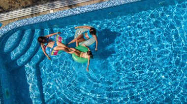 Yüzme havuzundaki aile yukarıdan insansız hava aracı görüntüsü, mutlu anne ve çocuklar şişme halka çöreklerle yüzüyor ve aile tatilinde suda eğleniyor, tatil beldesinde tropikal tatiller
