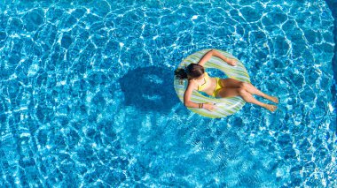 Hava dron görünümünü yüzme havuzundan yukarıdaki küçük kız, çocuğu şişme halka çörek üzerinde yüzüyor, çocuğu olan aile tatil tatil su eğlenceli mavi