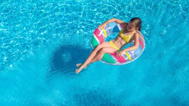 Hava dron görünümünü yüzme havuzundan yukarıdaki küçük kız, çocuğu şişme halka çörek üzerinde yüzüyor, çocuğu olan aile tatil tatil su eğlenceli mavi