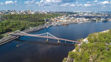 Kiev şehrinin yukarıdan havadan görünüşü, Kyiv silüeti, tepeler, yaya parkı köprüsü ve baharda Dinyeper nehri şehri, Ukrayna