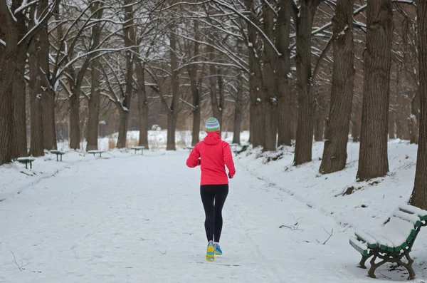 Winter running in park: happy active woman runner jogging in snow, outdoor sport and fitness concept
