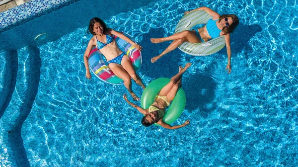 Yüzme havuzundaki aile yukarıdan insansız hava aracı görüntüsü, mutlu anne ve çocuklar şişme halka çöreklerle yüzüyor ve aile tatilinde suda eğleniyor, tatil beldesinde tropikal tatiller