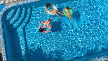 Yüzme havuzundaki aile yukarıdan insansız hava aracı görüntüsü, mutlu anne ve çocuklar şişme halka çöreklerle yüzüyor ve aile tatilinde suda eğleniyor, tatil beldesinde tropikal tatiller