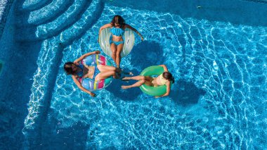 Yüzme havuzundaki aile yukarıdan insansız hava aracı görüntüsü, mutlu anne ve çocuklar şişme halka çöreklerle yüzüyor ve aile tatilinde suda eğleniyor, tatil beldesinde tropikal tatiller
