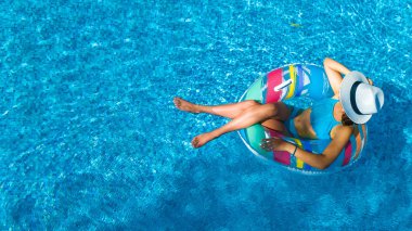Beautiful girl in hat in swimming pool aerial top view from above, young woman relaxes and swims on inflatable ring donut and has fun in water on family vacation, tropical holiday resort