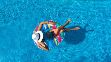 Beautiful girl in hat in swimming pool aerial top view from above, young woman relaxes and swims on inflatable ring donut and has fun in water on family vacation, tropical holiday resort