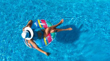 Beautiful girl in hat in swimming pool aerial top view from above, young woman relaxes and swims on inflatable ring donut and has fun in water on family vacation, tropical holiday resort