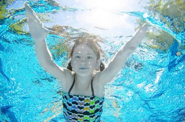 Çocuk yüzme havuzunda su altında yüzüyor, mutlu aktif genç kız dalıyor ve su altında eğleniyor, çocuk fitness ve tatil beldesinde aile tatilinde spor yapıyor.