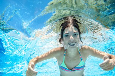 Çocuk yüzme havuzunda su altında yüzüyor, mutlu aktif genç kız dalıyor ve su altında eğleniyor, çocuk fitness ve tatil beldesinde aile tatilinde spor yapıyor.