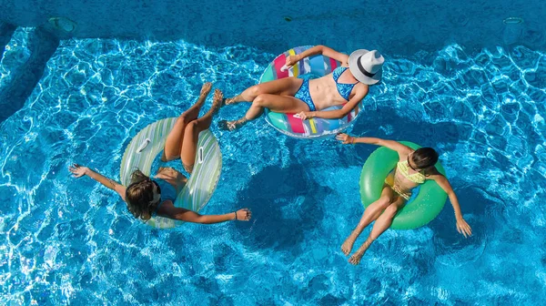 Family in swimming pool aerial drone view from above, happy mother and kids swim on inflatable ring donuts and have fun in water on family vacation, tropical holidays on resort