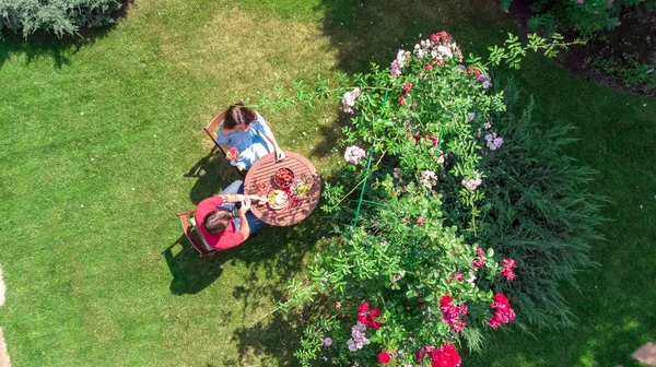 Young couple enjoying food and wine in beautiful roses garden on romantic date, aerial top view from above of man and woman eating and drinking together outdoors in park