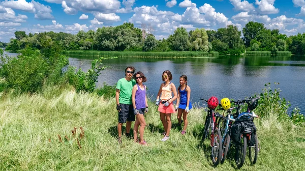 Family on bikes cycling outdoors, active parents and kids on bicycles, aerial top view of happy family with children relaxing near beautiful river from above, weekend and vacation sport and fitness concept