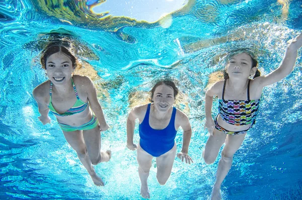 Family swims in pool underwater, happy active mother and children have fun under water, fitness and sport with kids on summer vacation on resort