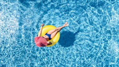 Yüzme havuzunda şapkalı güzel bir kadın yukarıdan havuz manzaralı, bikinili genç bir kız şişme yüzüklü çörek yiyor ve aile tatilinde suda eğleniyor, tropikal tatil beldesinde.