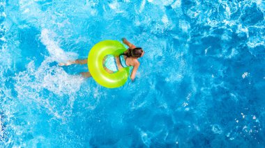 Yüzme havuzundaki aktif genç kız yukarıdan havuz manzaralı, çocuk gevşiyor ve şişme halka donutla yüzüyor ve aile tatilinde suda eğleniyor, tropikal tatil beldesi