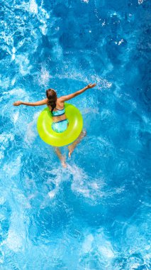 Yüzme havuzundaki aktif genç kız yukarıdan havuz manzaralı, çocuk gevşiyor ve şişme halka donutla yüzüyor ve aile tatilinde suda eğleniyor, tropikal tatil beldesi