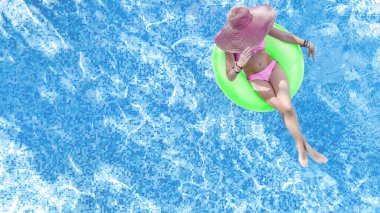 Yüzme havuzunda şapkalı güzel bir kadın yukarıdan havuz manzaralı, bikinili genç bir kız şişme yüzüklü çörek yiyor ve aile tatilinde suda eğleniyor, tropikal tatil beldesinde.