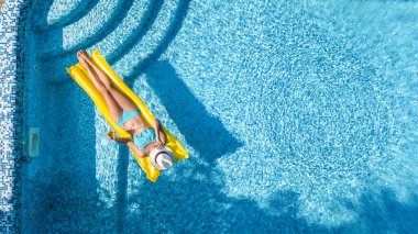 Yüzme havuzunda dinlenen güzel bir genç kız, şişme yatakta yüzen ve aile tatilinde suda eğlenen bir kadın, tropikal tatil beldesi, yukarıdan drone manzarası