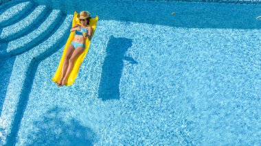 Yüzme havuzunda dinlenen güzel bir genç kız, şişme yatakta yüzen ve aile tatilinde suda eğlenen bir kadın, tropikal tatil beldesi, yukarıdan drone manzarası