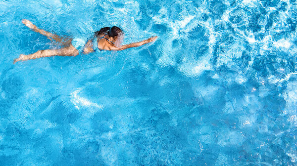 Active girl in swimming pool aerial drone view from above, young woman swims in blue water, tropical vacation, holiday on resort concept