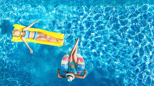 上からのスイミングプールの空中ドローンビューの子供たち 幸せな子供たちはインフレータブルリングドーナツとマットレスで泳ぐ アクティブな女の子は休日のリゾートで家族の休暇で水の中で楽しみを持っています — ストック写真