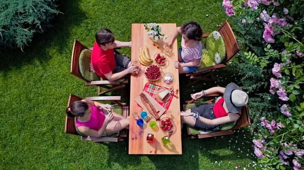 Family and friends eating together outdoors on summer garden party. Aerial view of table with food and drinks from above. Leisure, holidays and picnic concept