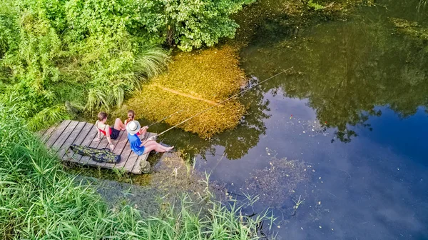 Happy family and friends fishing together outdoors near lake in summer, aerial top view from above
