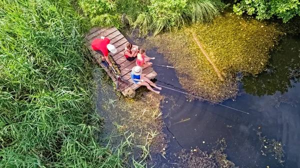 Happy family and friends fishing together outdoors near lake in summer, aerial top view from above