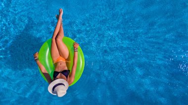 Havuz manzaralı şapkalı güzel bir kadın bikinili genç bir kız gevşiyor ve yüzükten şişme donutla yüzüyor ve tatilde suda eğleniyor.