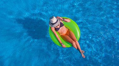 Havuz manzaralı şapkalı güzel bir kadın bikinili genç bir kız gevşiyor ve yüzükten şişme donutla yüzüyor ve tatilde suda eğleniyor.