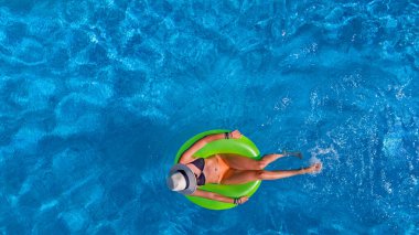 Havuz manzaralı şapkalı güzel bir kadın bikinili genç bir kız gevşiyor ve yüzükten şişme donutla yüzüyor ve tatilde suda eğleniyor.