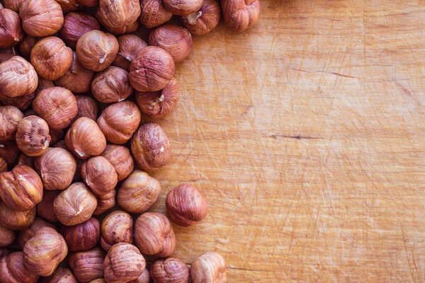 Round, large hazelnuts on an old, wooden, kitchen board. On the tree there are scratches, marks from the knife. Home cooking, vegetarian food, diet.
