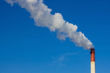 Açık mavi gökyüzünün arka planında büyük bir pipo tüttürür. Atmosfer kirliliği, kötü ekoloji, çevreye zarar.