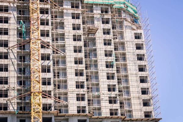 Urban construction, construction of real estate, condominium. Against the blue sky there is a huge building under construction. Bright sunlight, view from below.