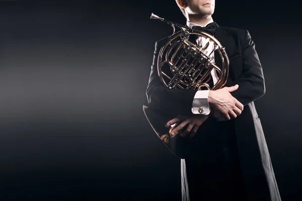 Classical musician with french horn music instrument. Elegant man hornist in tuxedo portrait.