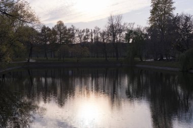 Sonbahar boyunca şehir parkında günbatımında yansımalar ve düşen yapraklarla dolu bir göl. Doğa, mevsimlik