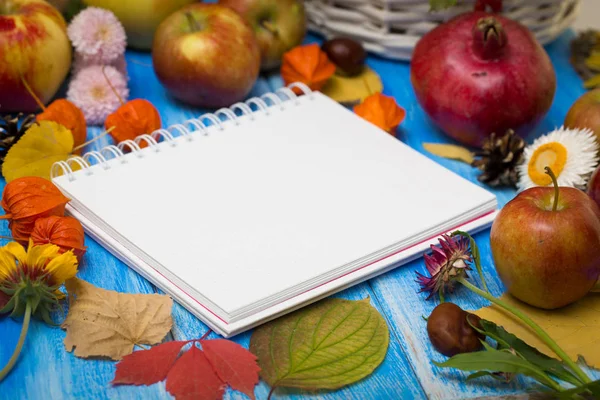 Autumn bright background. Notebook for the inscription. Flowers, leaves and fruits on a blue wooden background. Background for the autumn holidays and thanksgiving day.